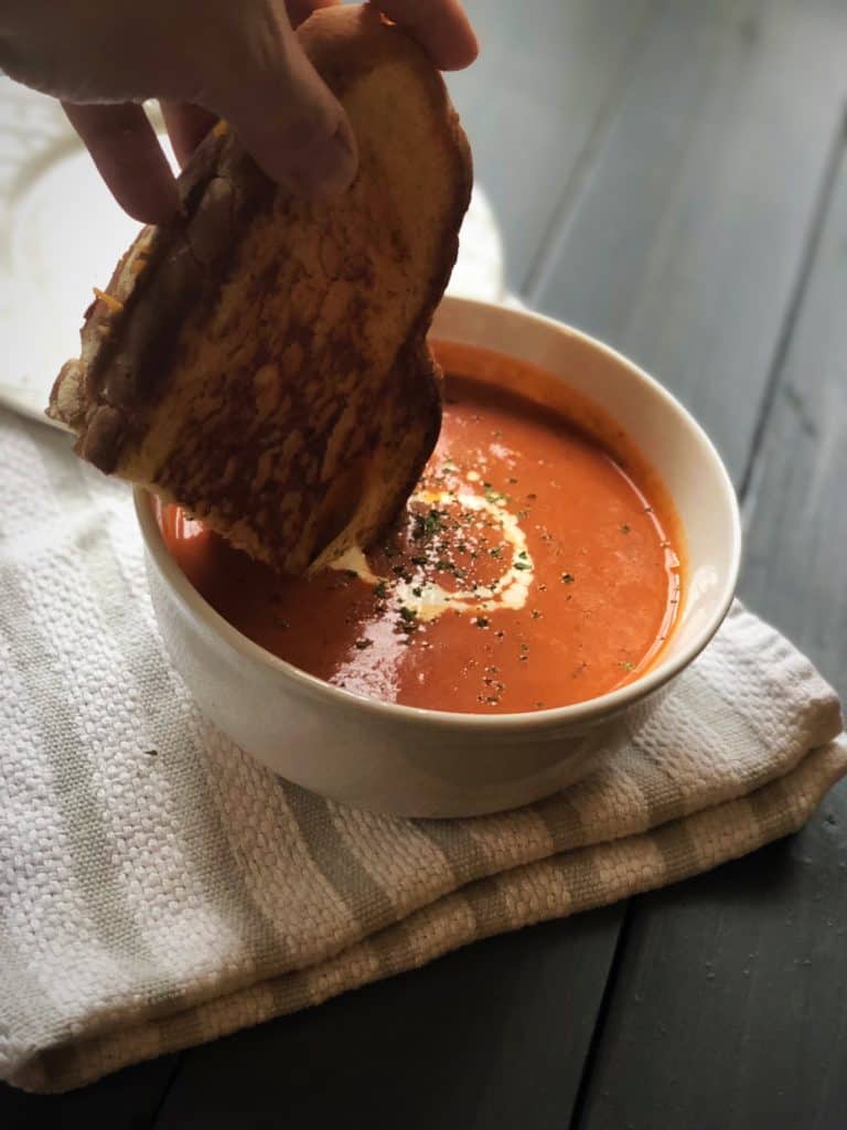 grilled cheese dipping into creamy tomato basil soup