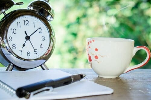a clock, journal and coffee mug on a table outside