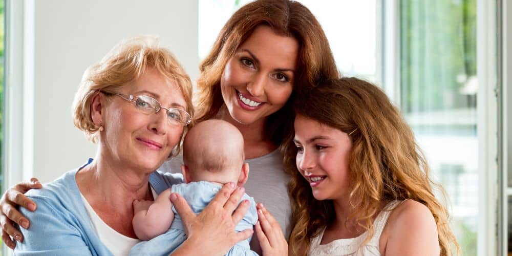 three generation of women posing for a photograph - one older white woman, one middle-aged white woman, a white little girl and a white baby