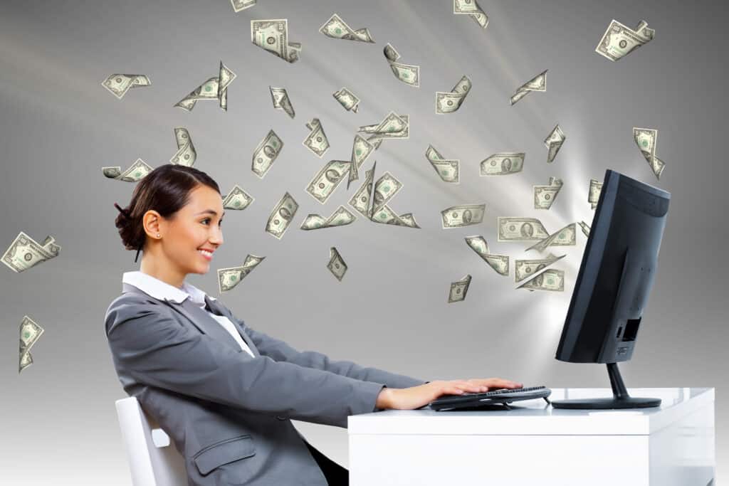 an asian woman working at computer with money flying out of it