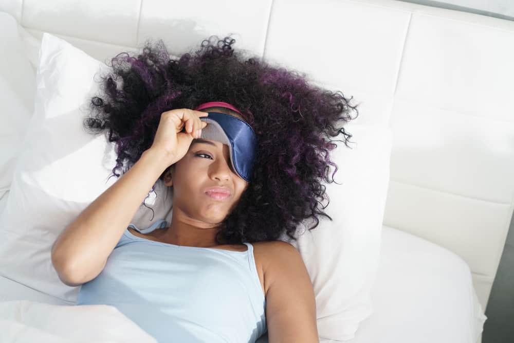 black woman waking up in a white bed while taking her sleep mask off