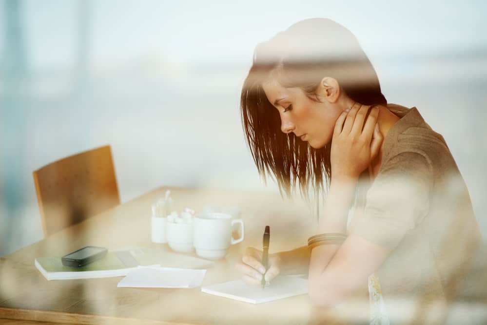 brunette woman writing about self love journal prompts at a diner