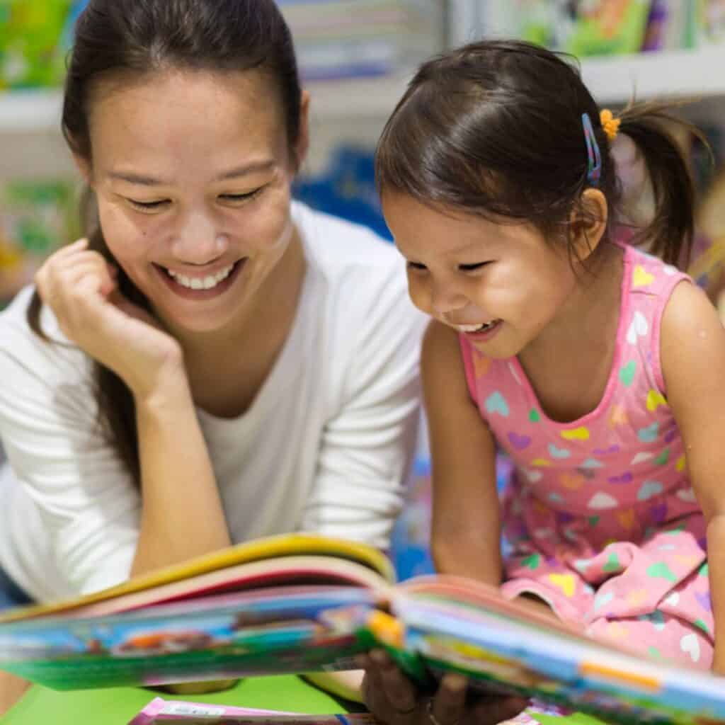 Asian mom and daughter reading a book at the library together