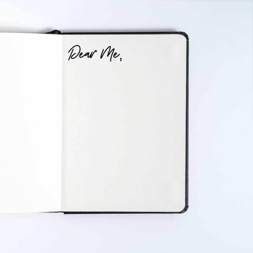 black journal opened to a black page that says "dear me" that will be used for write self love journal prompts